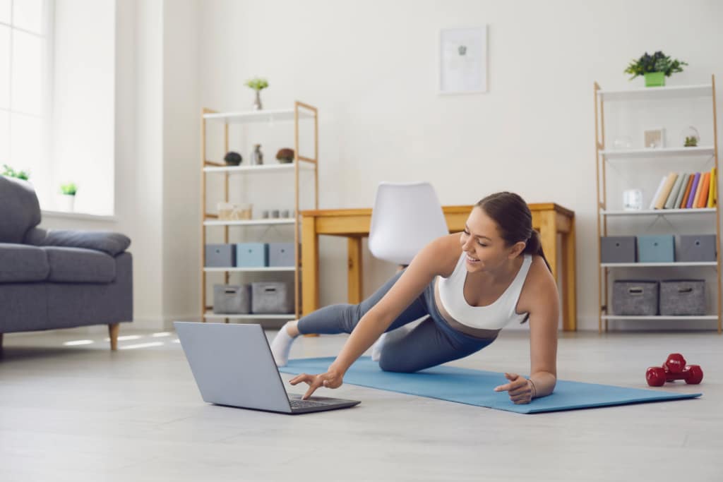 woman on a yoga mat on the floor with a laptop in front of her