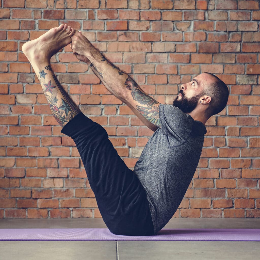 Man with a beard on a pilates mat doing a V sit and touching his fingers to his toes