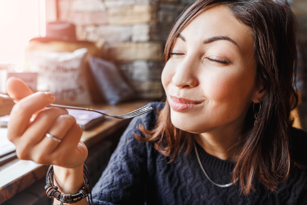 young asian woman sitting in a cafe and holding a fork looking pleased