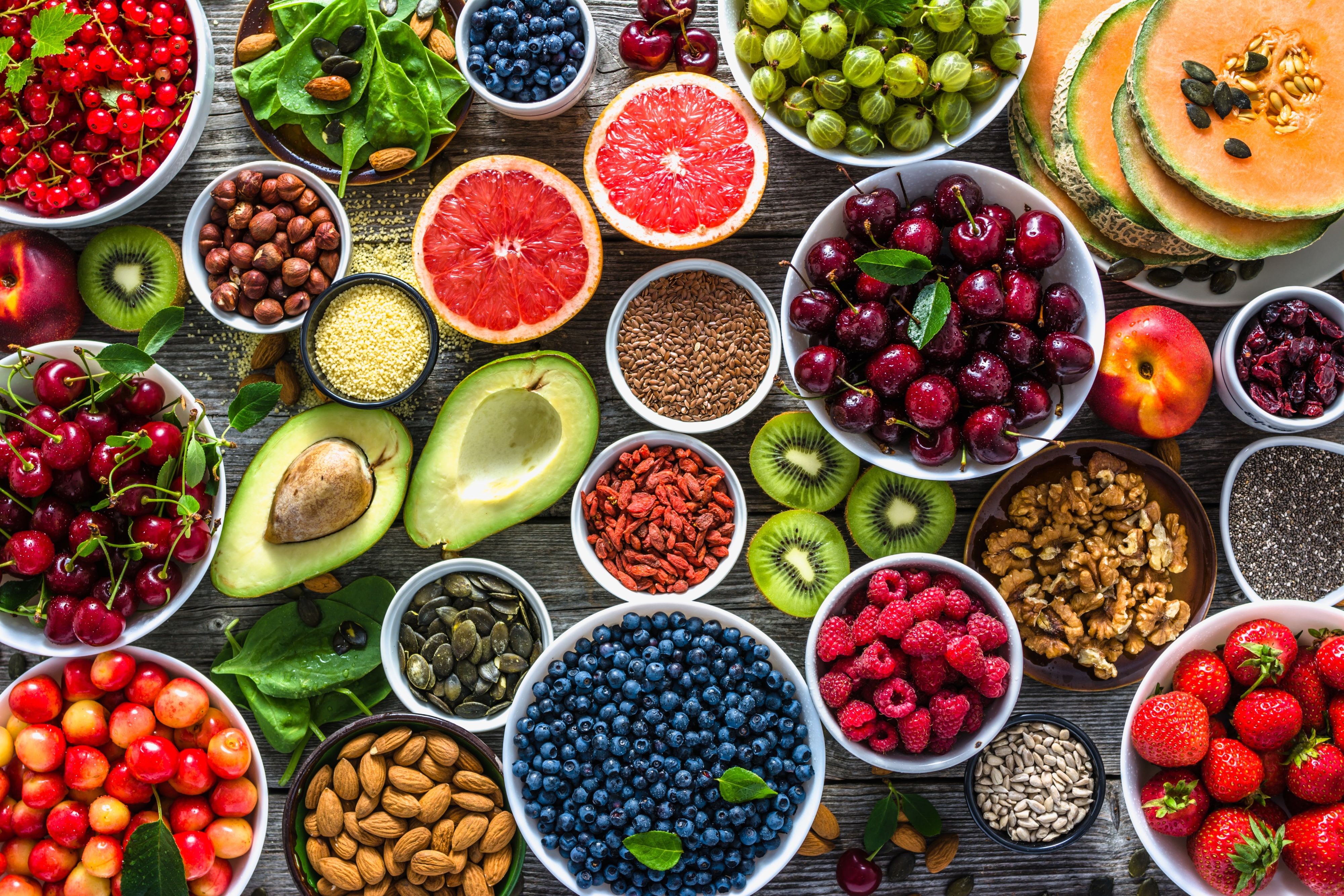 A selection of healthy superfoods like fruits, vegetables, nuts, and seeds, including avocado, cherries, goji berries, and blueberries