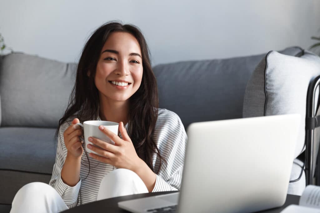 woman holding a mug and looking at her laptop in a living room